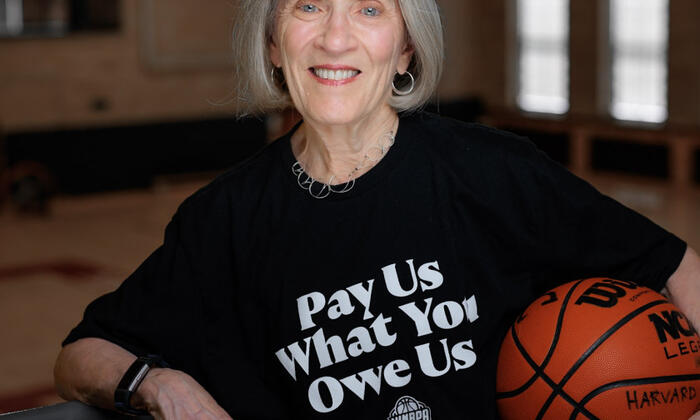 Claudia Goldin wearing a shirt reading "pay us what you owe us" and holding a basketball. 
