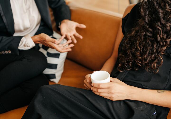 A close up of two people sitting on a couch engaged in deep conversation.