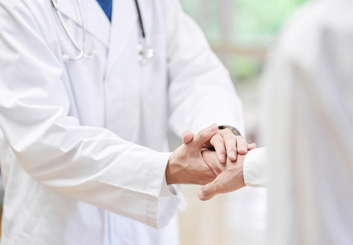 A doctor in a white coat shakes hands with a patient. 