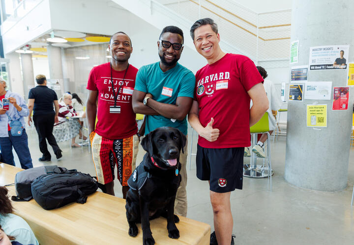 Three male members of the Harvard community posing for a photo with Sasha, the HUPD community engagement dog.