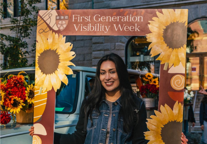 A Harvard student posing with a large cardboard cut out frame which reads “FGLI Visibility Week.”