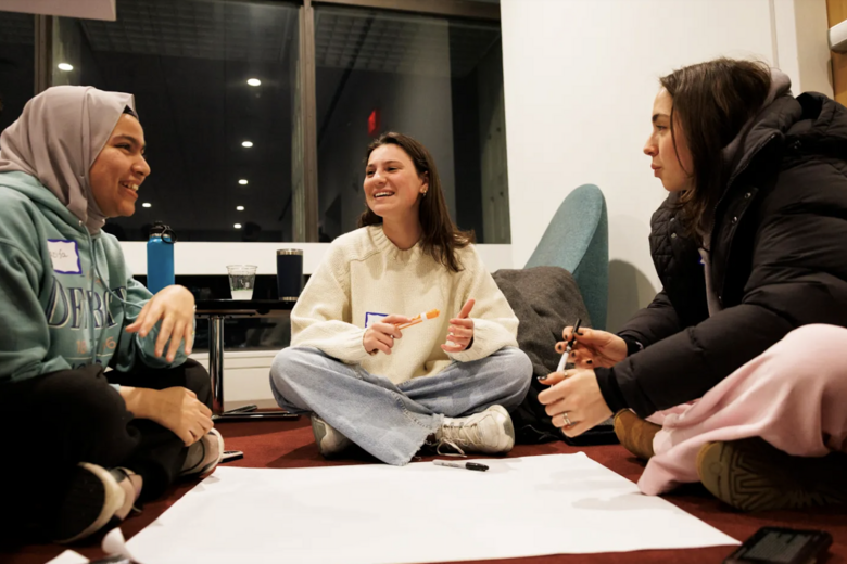 Three students sitting on the ground and working together during an event. 