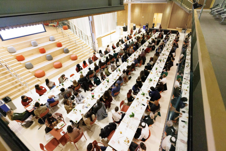 An aerial shot of approx. 150 attendees seated at long tables at the Across This Table interfaith dinner.