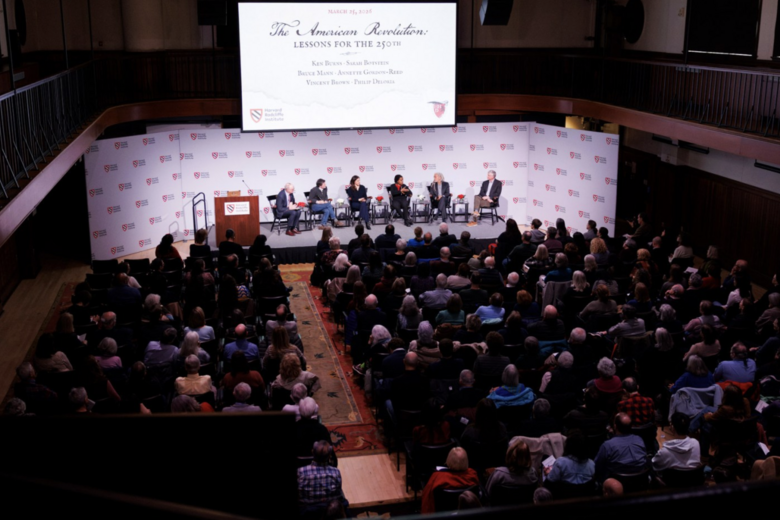 An aerial shot of the event The American Revolution: Lessons for the 250th, six speakers are on the stage and the seats are full. 