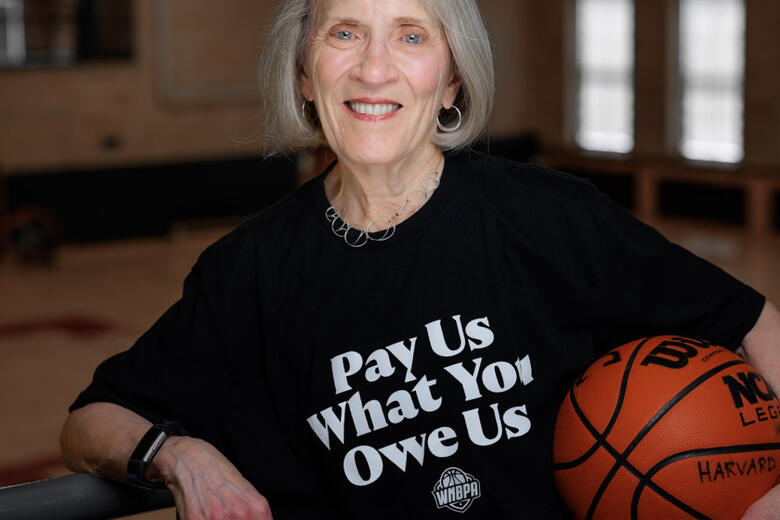Claudia Goldin wearing a shirt reading "pay us what you owe us" and holding a basketball. 