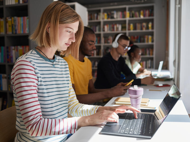 A woman sitting in a library, using her laptop.