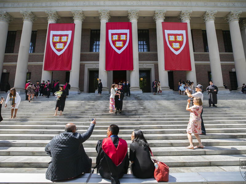 Widner Library with three "Veritas" banners and individuals looking at the entrance while seated on the front steps.
