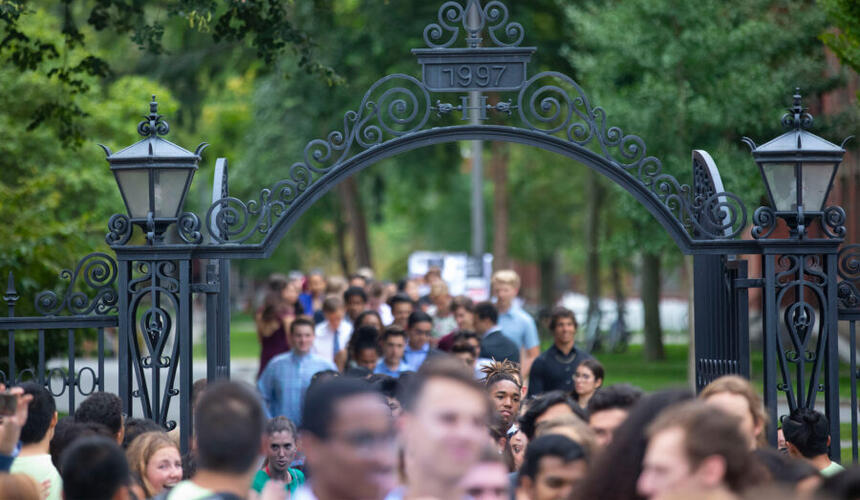 A close-up image of a Harvard gate with a crowd of people walking through it.