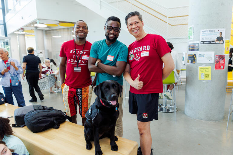 Three male members of the Harvard community posing for a photo with Sasha, the HUPD community engagement dog.