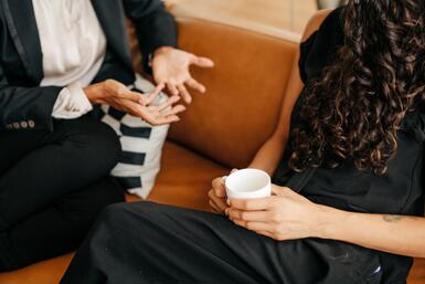 A close up of two people sitting on a couch engaged in deep conversation.