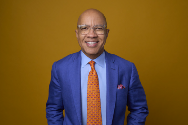 A waist up photo of Darren Walker, smiling in a bright blue suit and orange tie.